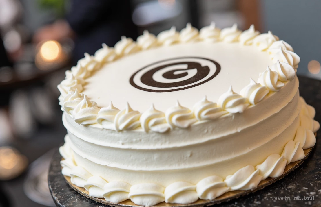 Een professionele foto van een aangepaste slagroomtaart met een bedrijfslogo op de frosting, getoond op een bedrijfsevenement. Moderne en strakke esthetiek.